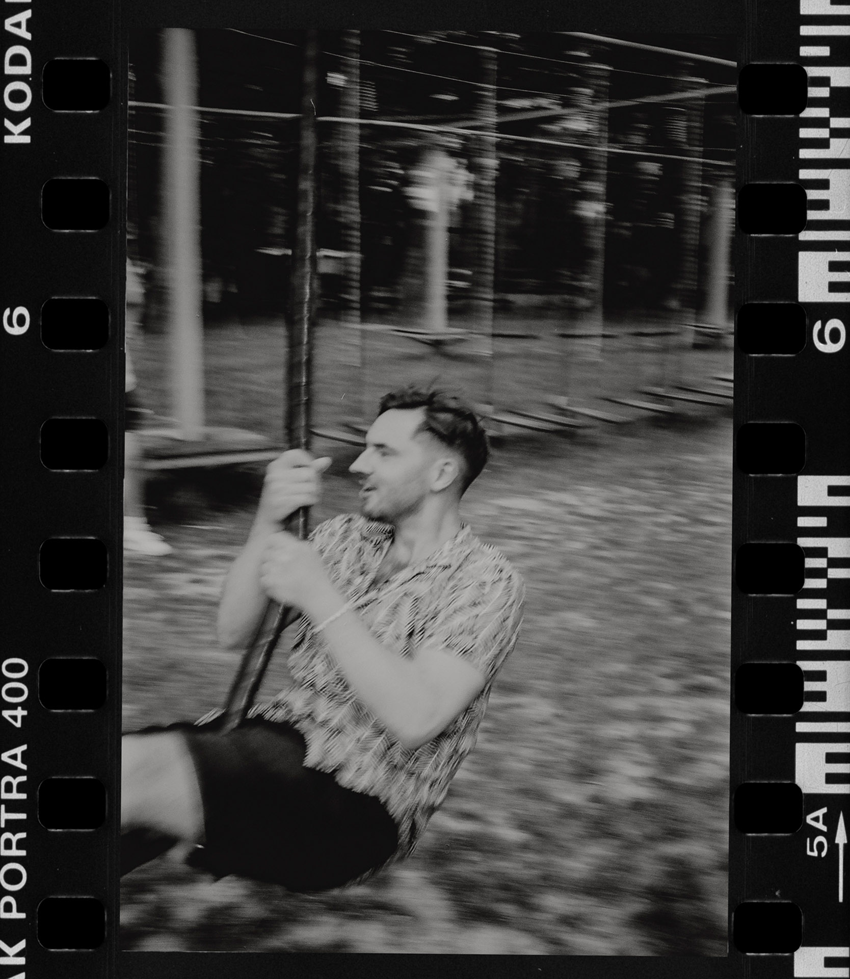 Skan analogowy przedstawiający Pana Młodego w niebieskim garniturze, z kieliszkiem w dłoni, idącego tyłem, otoczonego bujną zielenią w Małpim Gaju na terenie Sielsko Anielsko, sfotografowany przez Camera Folks – Wedding Photo & Video. To prawdziwe slow wedding!