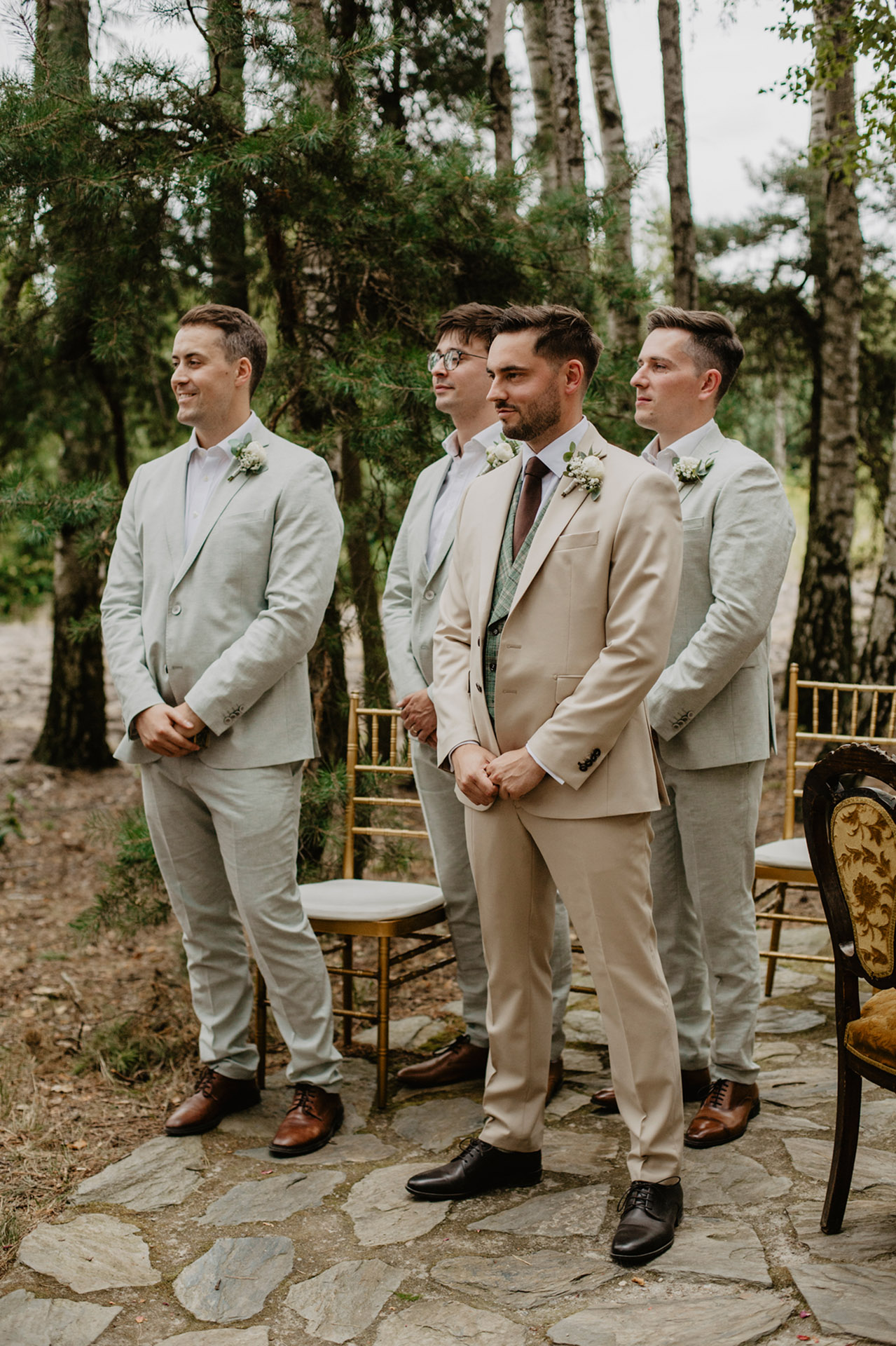 Pan Młody w beżowym garniturze, czekający na Pannę Młodą z trzema groomsmen w leśnym miejscu ceremonii w Sielsko Anielsko, sfotografowany przez Camera Folks – Wedding Photo & Video.