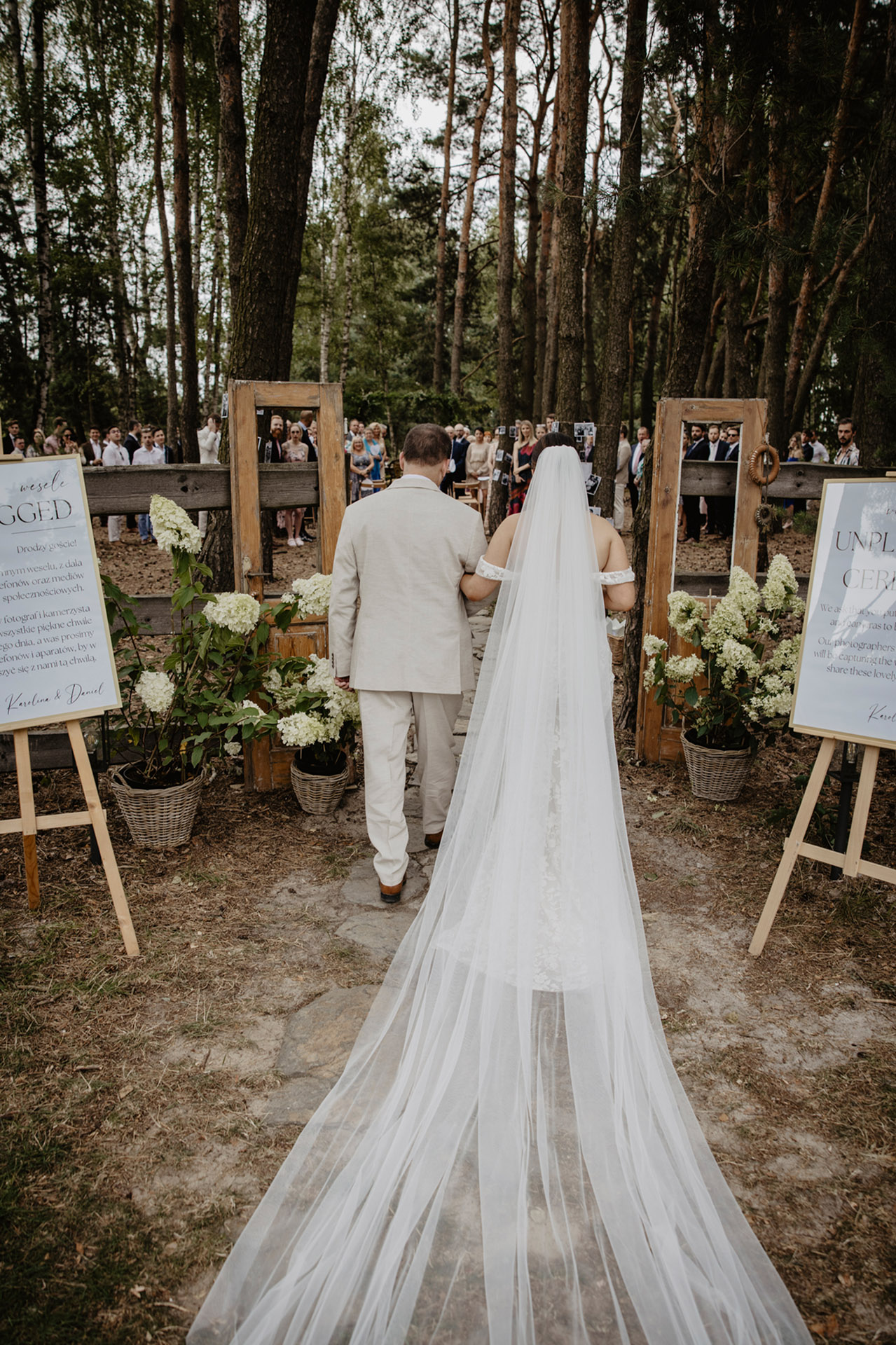 Panna Młoda w długim welonie idąca z tatą kamienną ścieżką w lesie Sielsko Anielsko, w drodze na ceremonię ślubną, sfotografowana przez Camera Folks – Wedding Photo & Video.