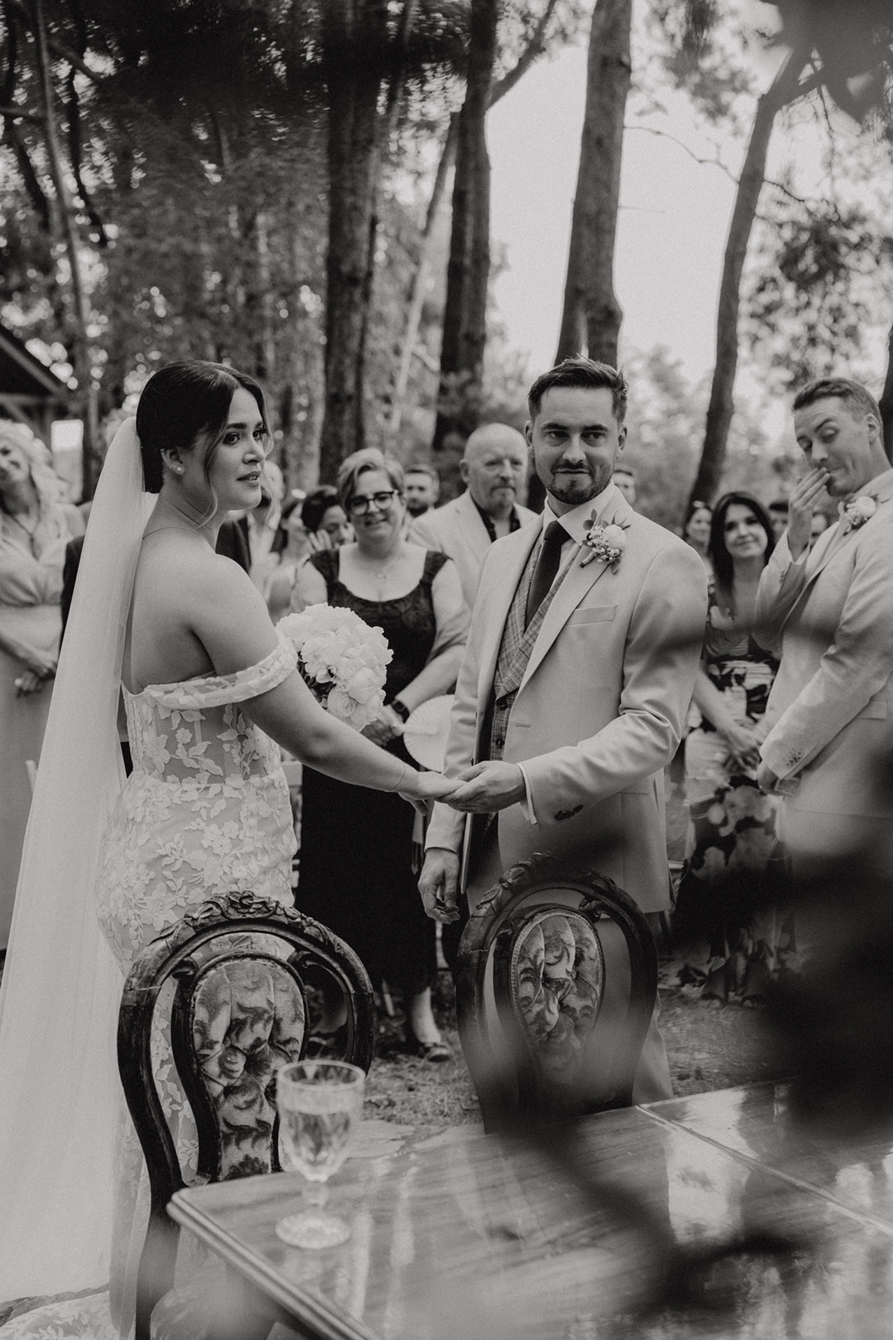 Para Młoda K&D trzymająca się za ręce podczas ceremonii zaślubin w Sielsko Anielsko, otoczona gośćmi i zielenią lasu, uchwycona przez Camera Folks – Wedding Photo & Video