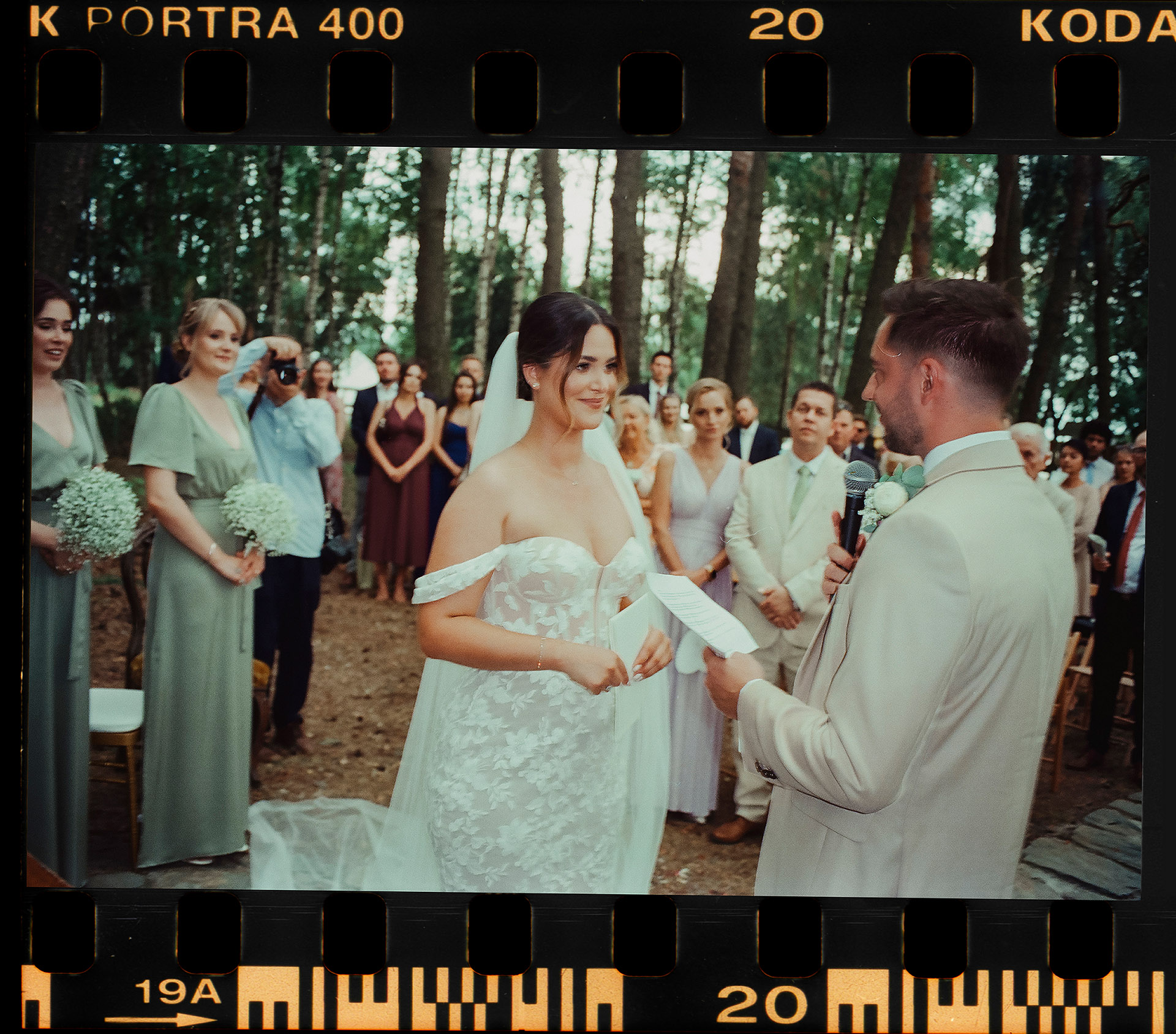 Analogowy skan przedstawiający Parę Młodą podczas ceremonii ślubnej w lesie Sielsko Anielsko, z Panną Młodą patrzącą na Pana Młodego czytającego śluby, sfotografowany przez Camera Folks – Wedding Photo & Video.