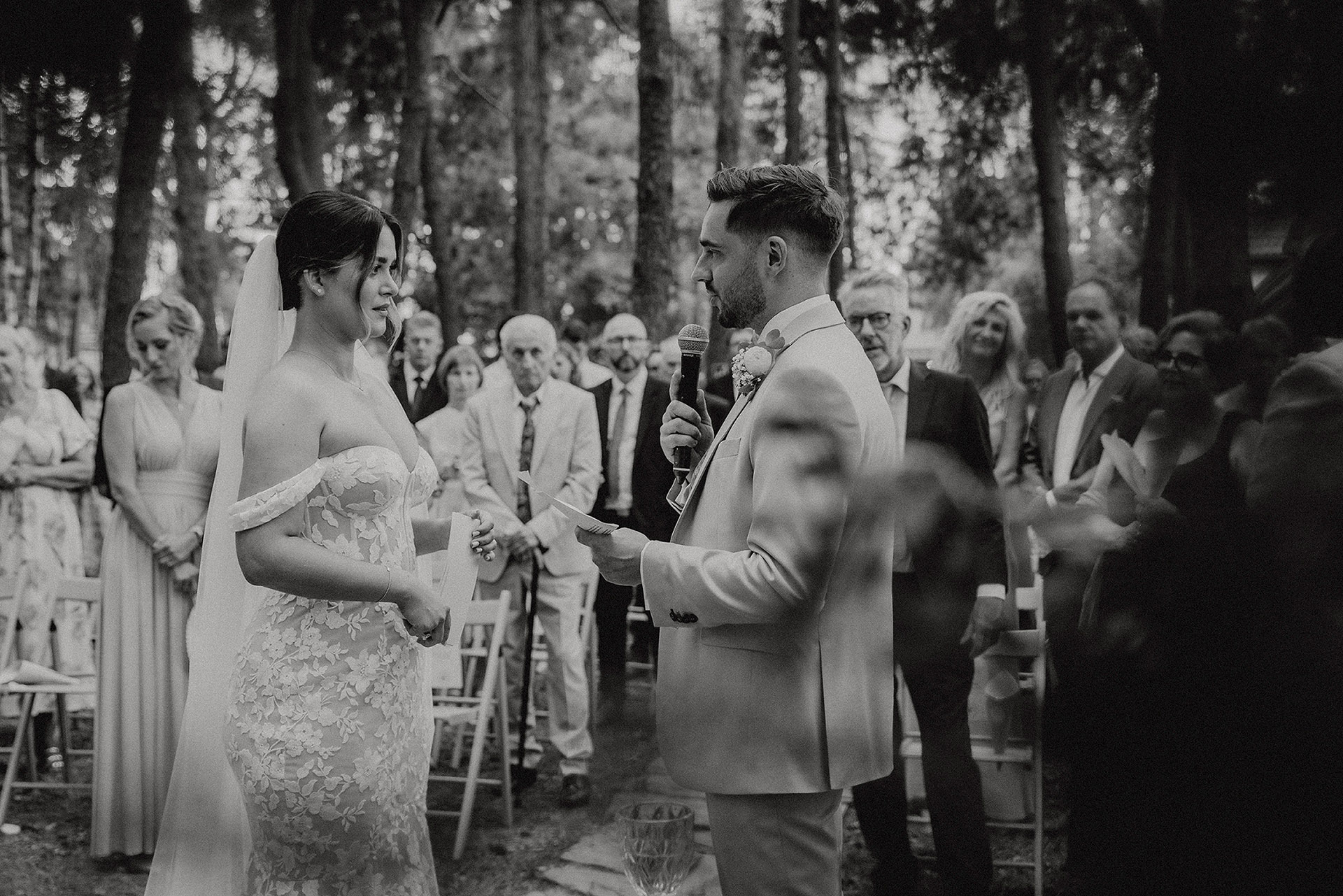 Pan Młody czytający osobistą przysięgę ślubną Pannie Młodej w otoczeniu gości podczas wzruszającej ceremonii w plenerze Sielsko Anielsko, sfotografowany przez Camera Folks – Wedding Photo & Video.