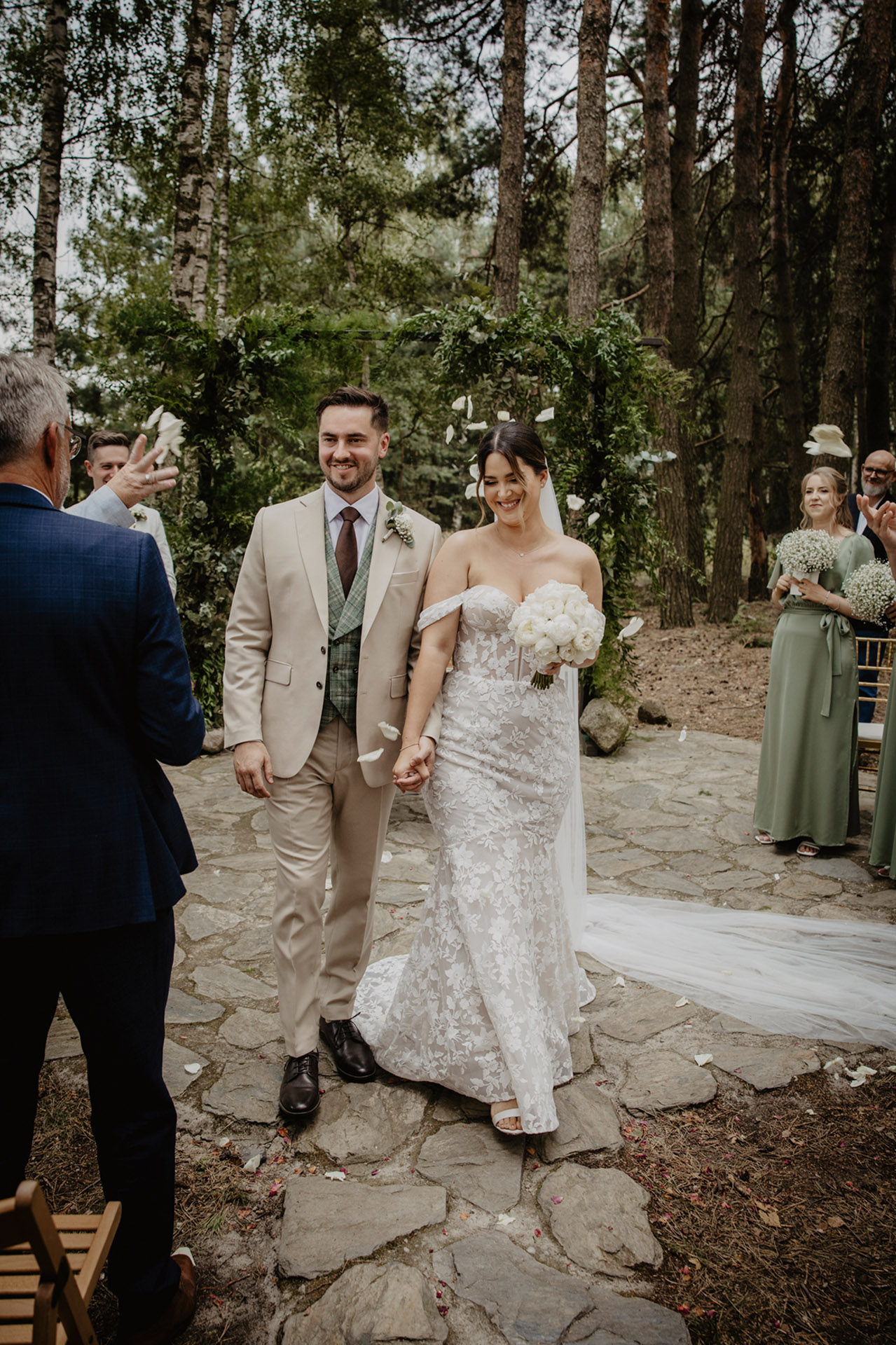 Para Młoda z uśmiechami idąca po ceremonii ślubnej w leśnym otoczeniu Sielsko Anielsko, z sypiącymi się płatkami, sfotografowana przez Camera Folks – Wedding Photo & Video.
