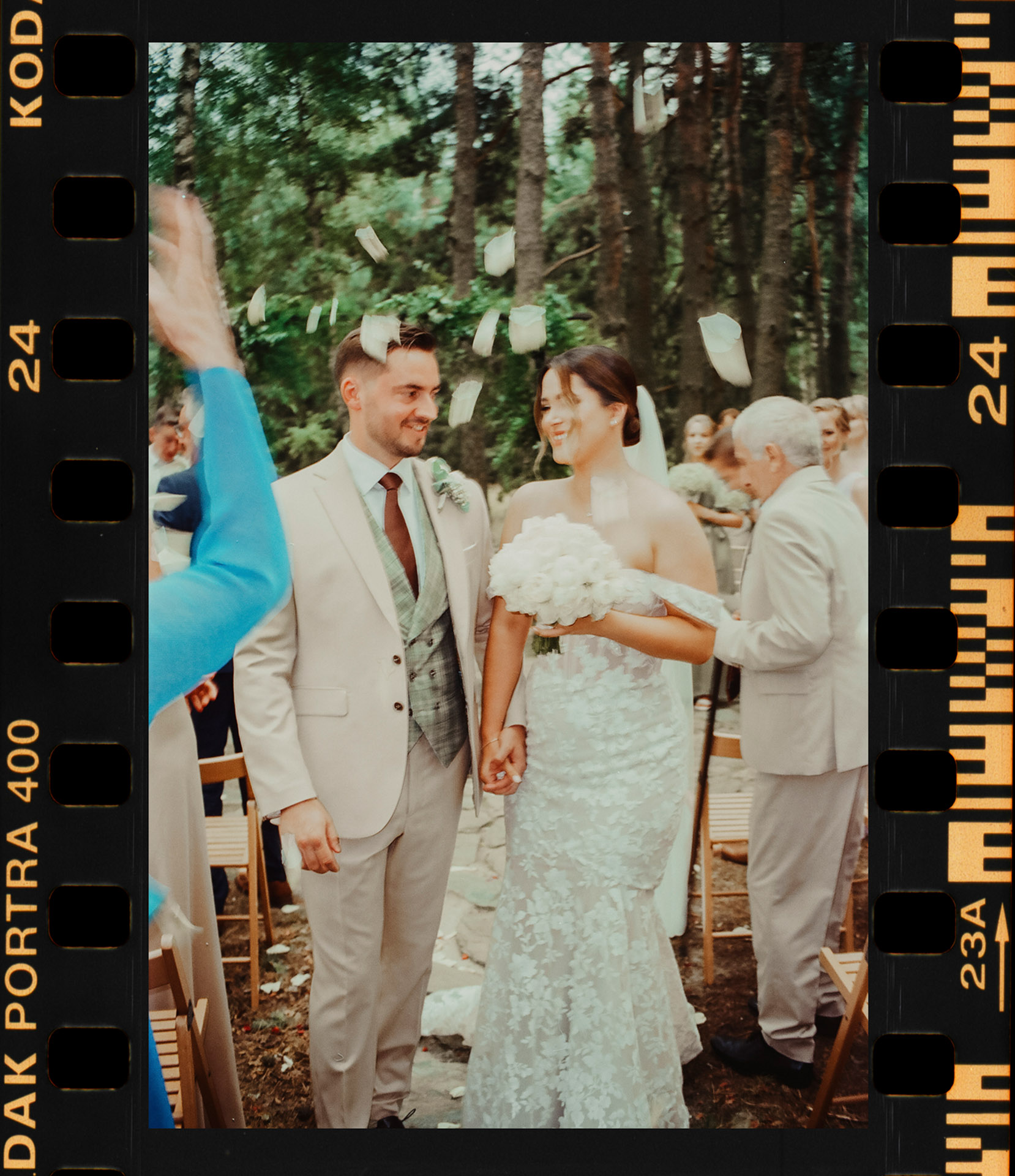 Analogowy skan z kliszy Kodak Portra 400 przedstawiający szczęśliwą Parę Młodą po ceremonii ślubnej, obsypywaną płatkami przez gości w leśnym otoczeniu Sielsko Anielsko, uwieczniony przez Camera Folks – Wedding Photo & Video.