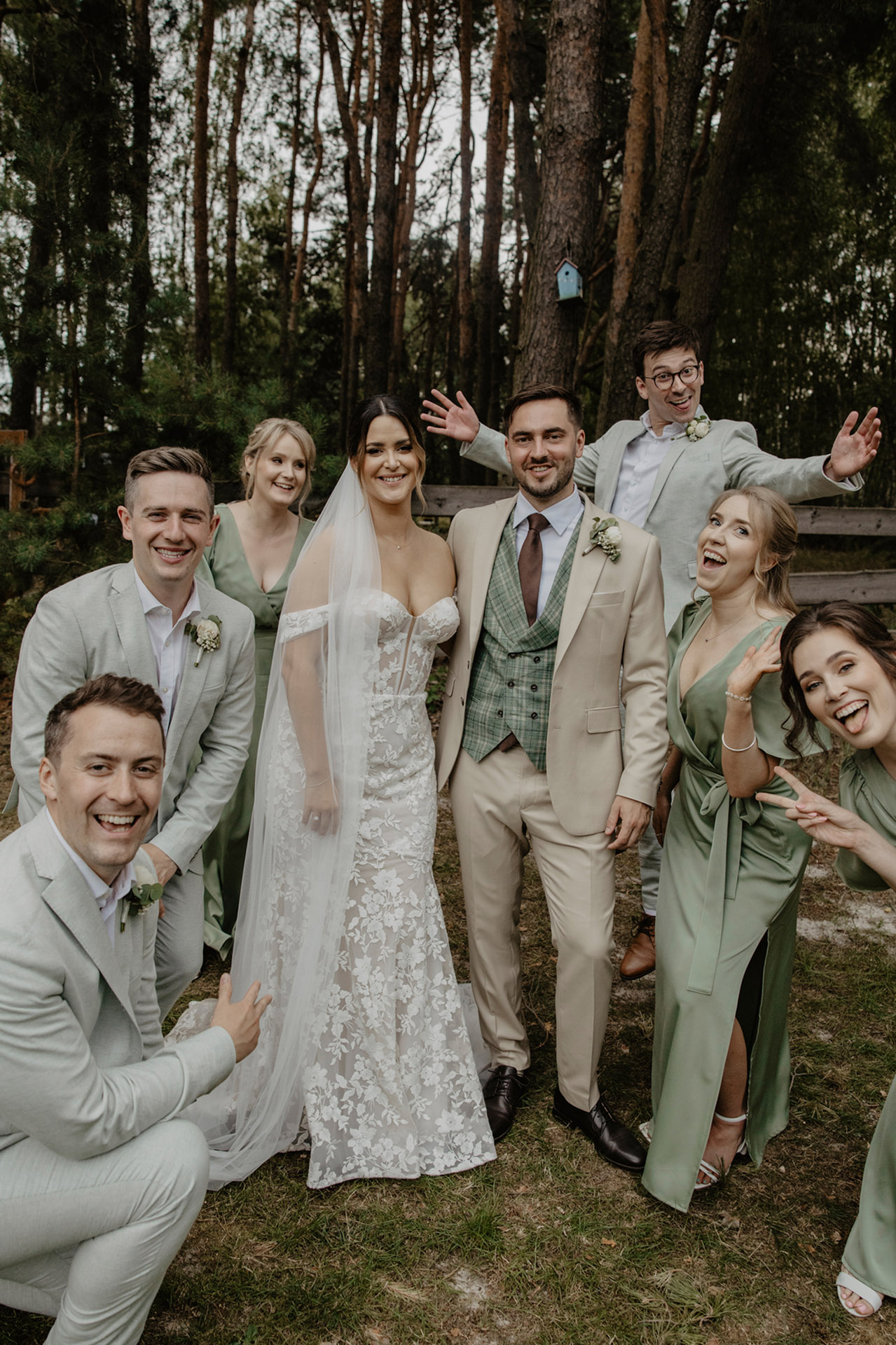 Klasyczne zdjęcie grupowe Panny Młodej i Pana Młodego z druhnami i drużbami, z kilkoma osobami żartobliwie pozującymi, np. z uszami królika, w plenerze Sielsko Anielsko, sfotografowane przez Camera Folks – Wedding Photo & Video.